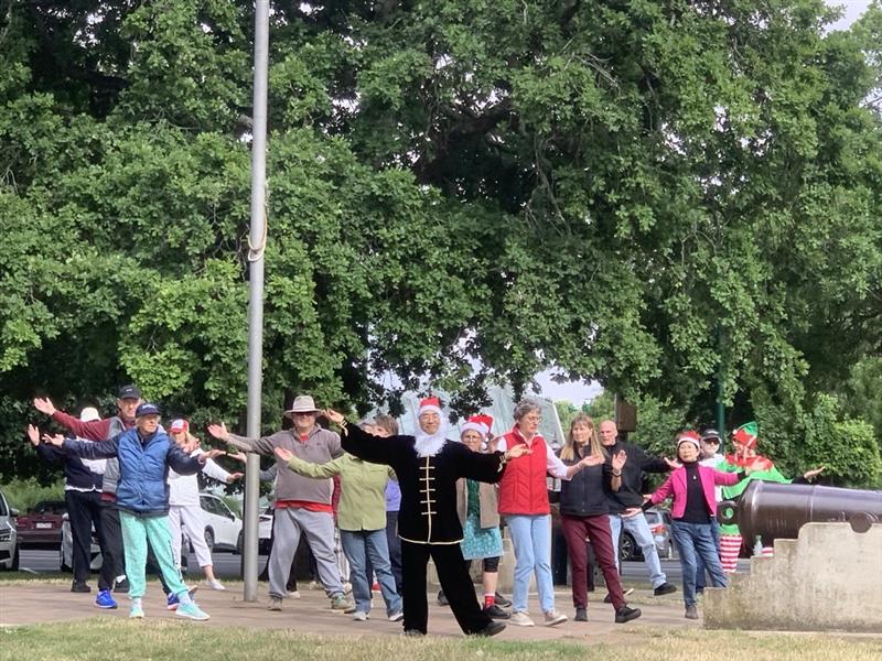 Un grupo de personas practicando Tai Chi en el parque, algunos disfrazados de Papá Noel y duendes. 