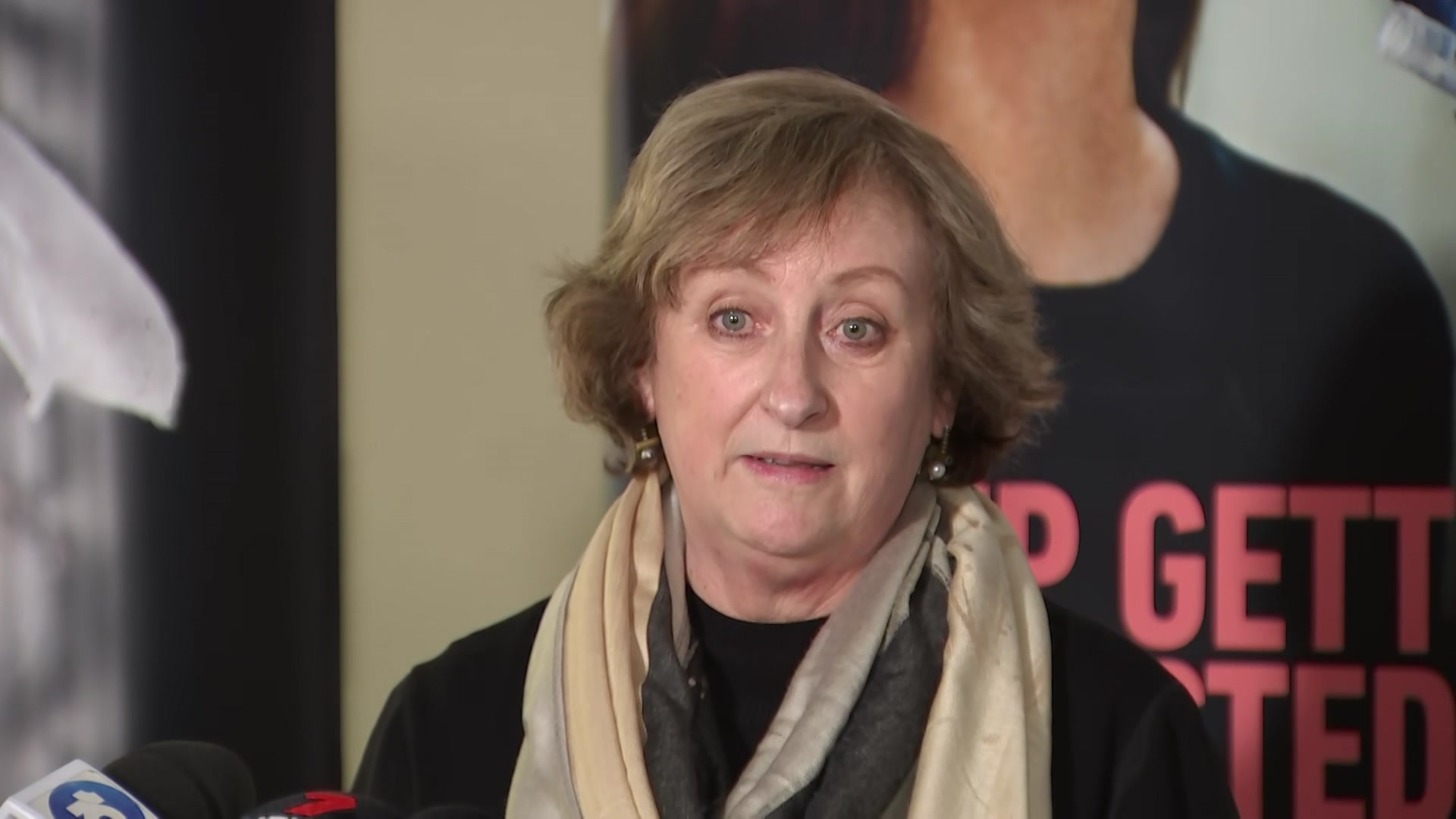 A woman with short brown hair wearing a beige scarf and a black top