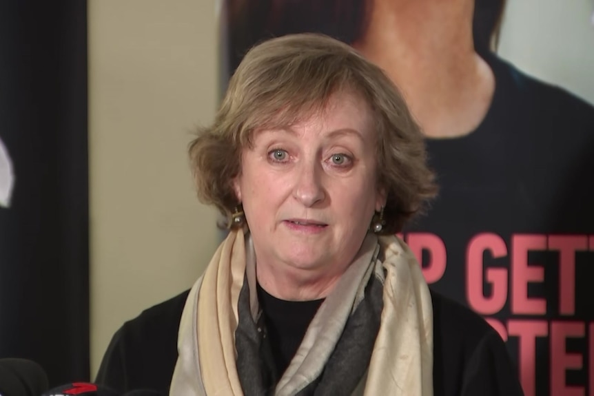 A woman with short brown hair wearing a beige scarf and a black top