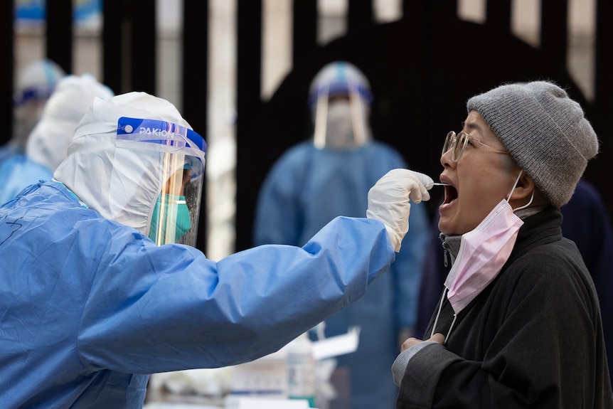 A woman opens her mouth while a health worker in full PPE puts a swab down her throat