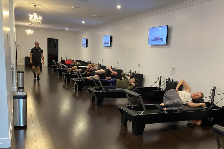 A row of people on pilates reformers as the instructor walks by