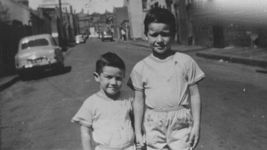 Two children stand side by side in the street.
