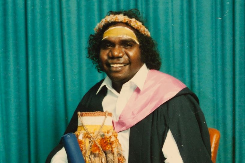 a smiling aboriginal man wearing teachers robes and a yellow headband
