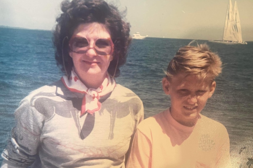 A mother and son pose for a photo on a boat with the water visible behind them.