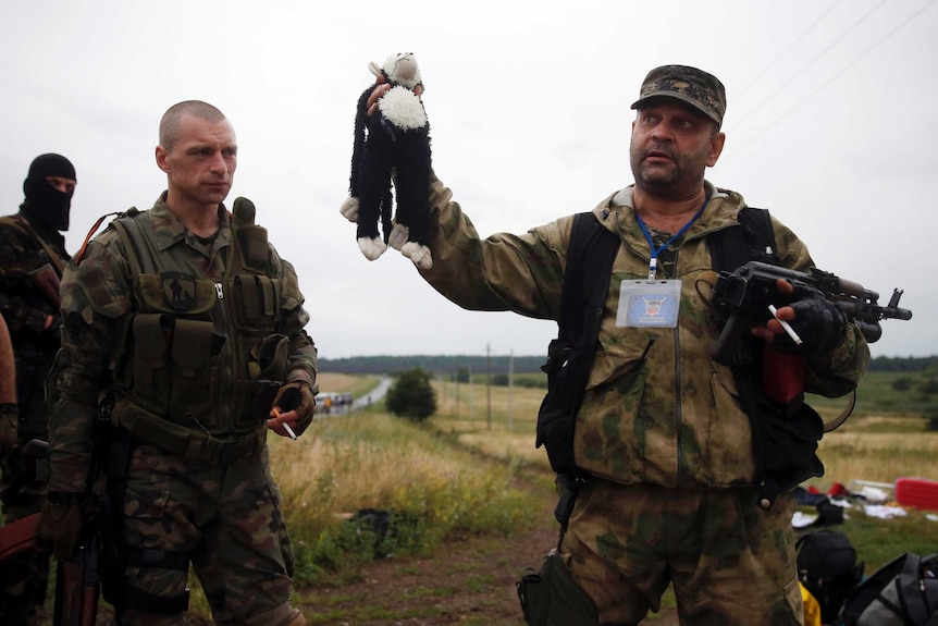 An armed pro-Russian separatist holding up a stuffed toy found at the MH17 crash site
