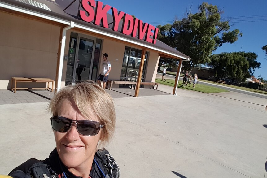 Denise Bess takes a selfie in front of a Skydive sign.