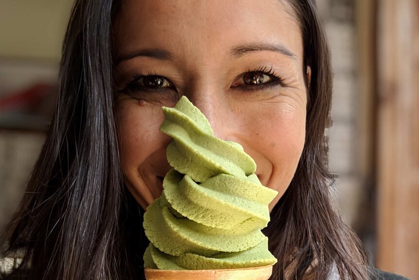 A woman smiles behind a green ice cream that covers half of her face.