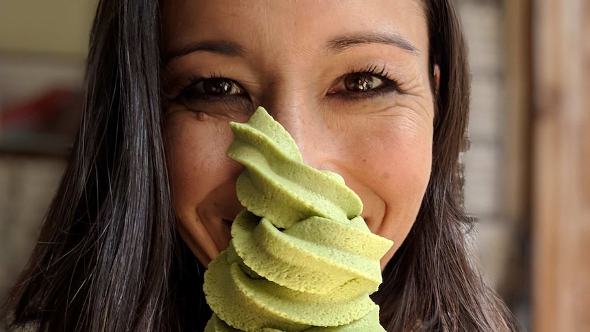 A woman smiles behind a green ice cream that covers half of her face.