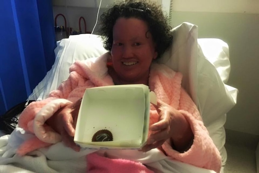 Carly Findlay in hospital bed showing off a cake that has been brought for her.