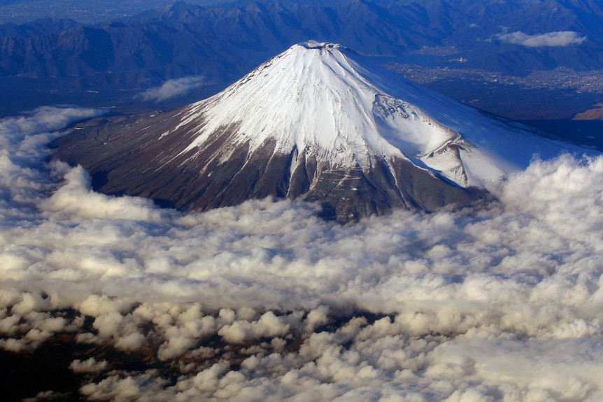 A conical mountain capped with snow rises from clouds.