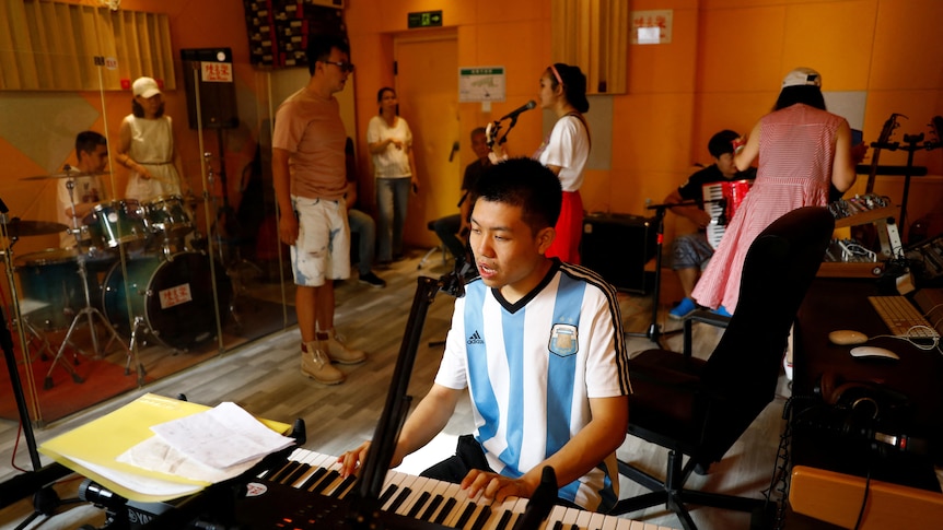 Mr Zu plays the keyboard as other students beind him sing and play the drums. 