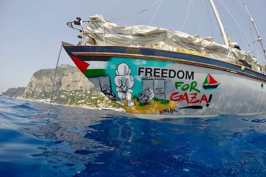 A yacht sitting in water, with graffiti-style artwork reading freedom for Gaza.