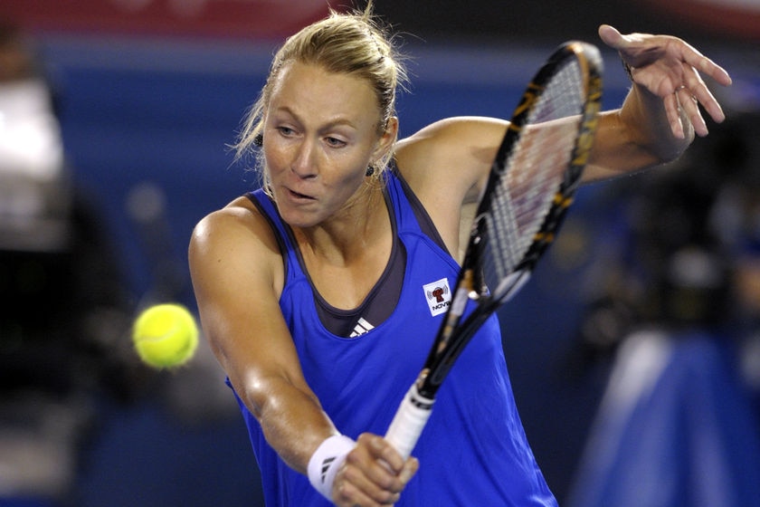 Alicia Molik wears a blue and black sleeveless tennis jersey, blonde hair tied back, about a hit a ball with racquet.