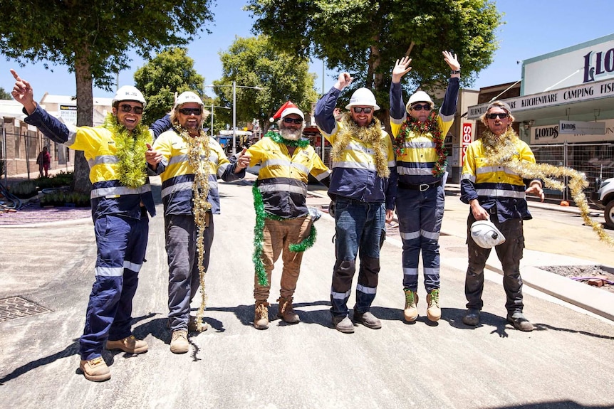 A group of six construction workers with tinsel and hands in the air standing in the middle of Bussell Highway