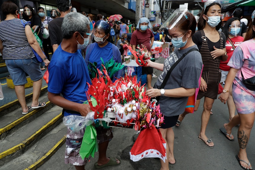 A woman wearing a face mask buys Christmas decorations at a busy market