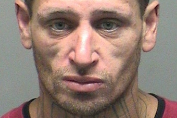 A man has a neutral expression in a mugshot. The word 'thug' is tattooed on his neck
