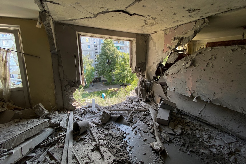 View inside destroyed apartment building with debris on the floor and large hole below the window.