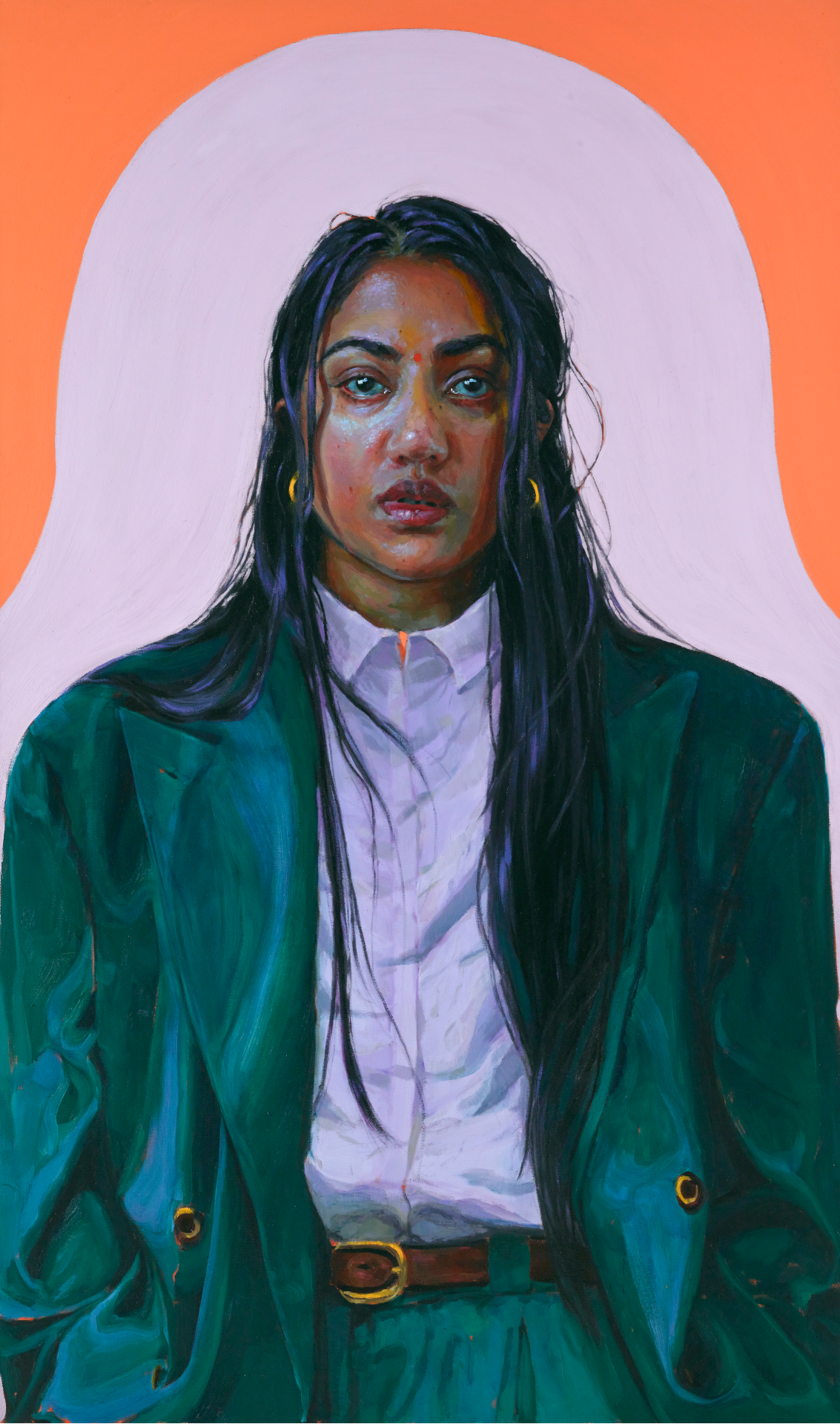 A self-portrait of Kirthna Selvaraj looking straight ahead and wearing an oversized green suit, with a white button-down