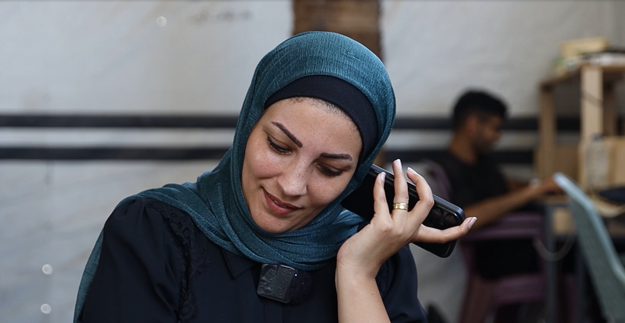 A woman in a blue hijab listens to her phone with it held to her ear