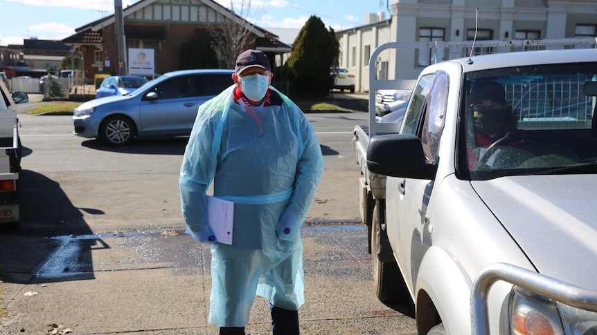 A person in protective gear stands outside a testing clinic.