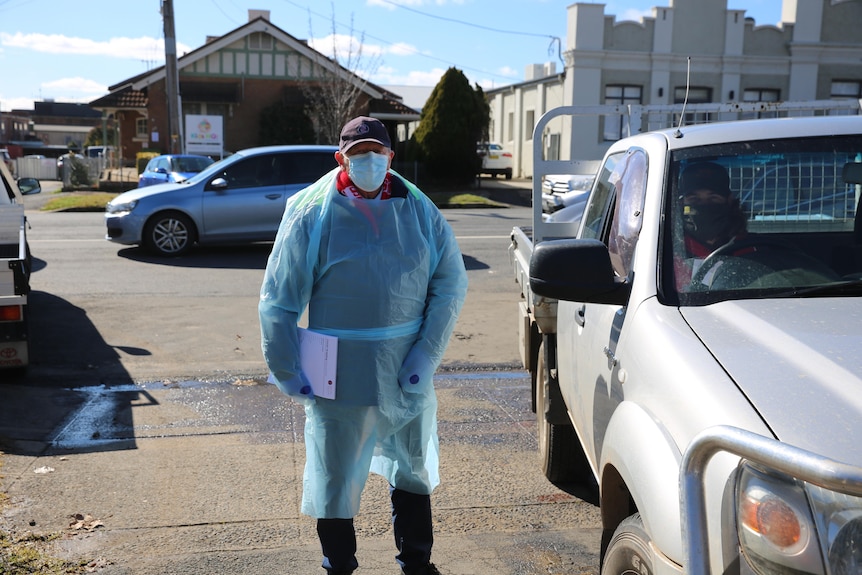 A person in protective gear stands outside a testing clinic.