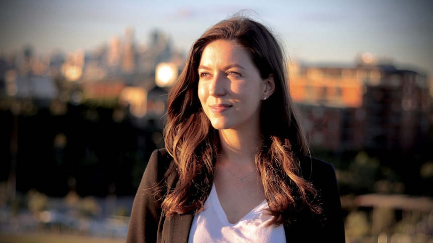 ETF investor Sharlie Raymond looks to her left. She's standing in a Sydney pack with a city backdrop.