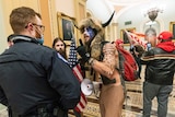 A man wearing an animal hat with horns and the US flag painted on his face confront a police office inside the Capitol.