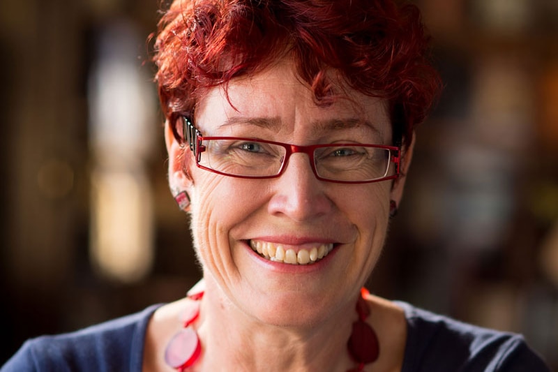 Women with red hair and glasses, dark blue shirt, smiling