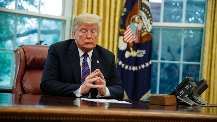 Donald Trump, at the Oval Office desk,  listens during a phone call with Enrique Pena Nieto. Eyes are closed, hands together.