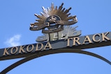 On a blue day, you see a closeup of a sign marking the Kokoda track with the ADF rising sun crown logo on top.