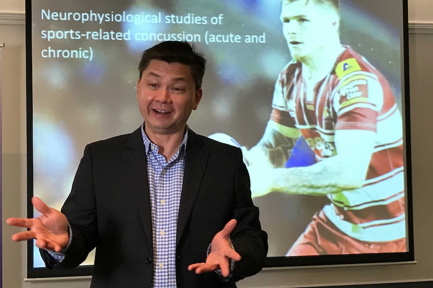 Dr Alan Pearce speaks in front of a slideshow featuring footballers.