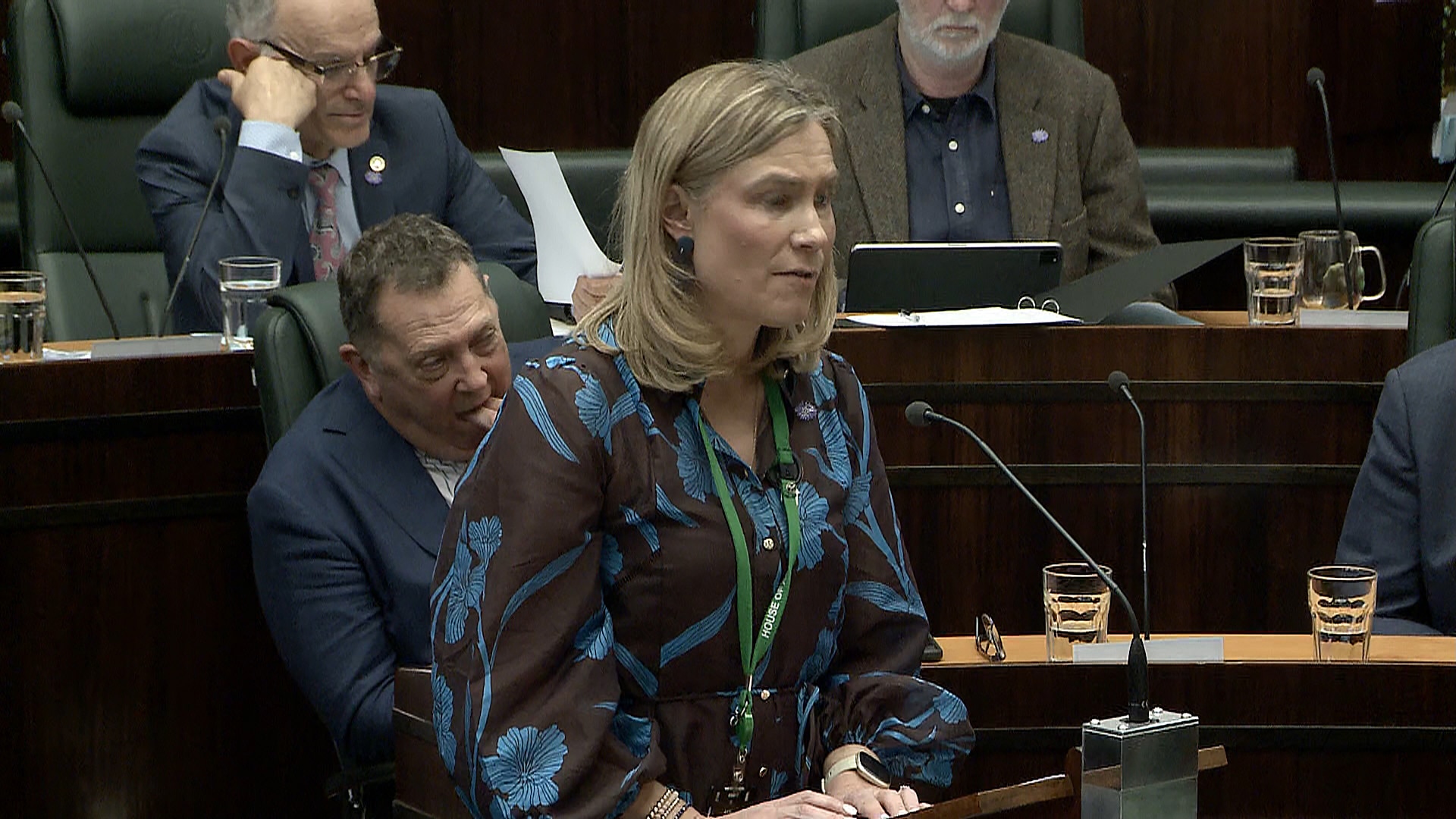 Kristie Johnston speaks in parliament as Gavin Pearce sits behind her and puts fingers in his mouth.