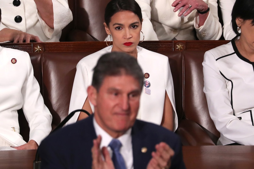 Alexandria Ocasio Cortez sitting behind Joe Manchin staring at the back of his head