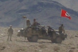 A red swastika flag above a small vehicle with soldiers present and Afghan hills in the background.