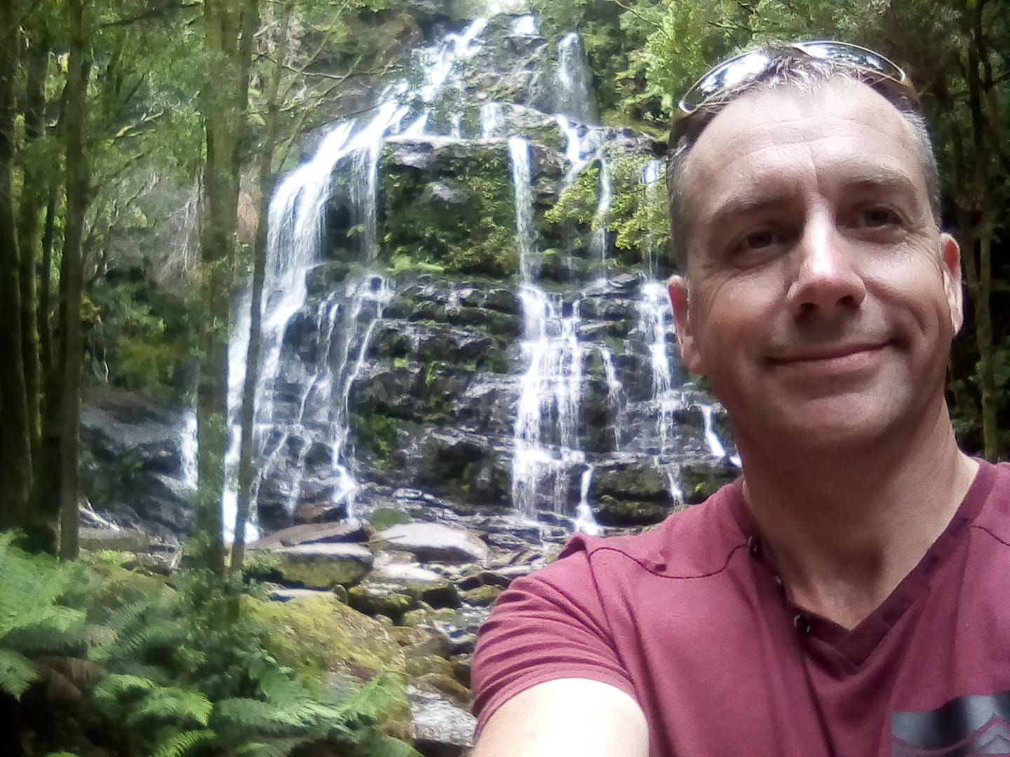 A man takes a selfie in front of a waterfall.