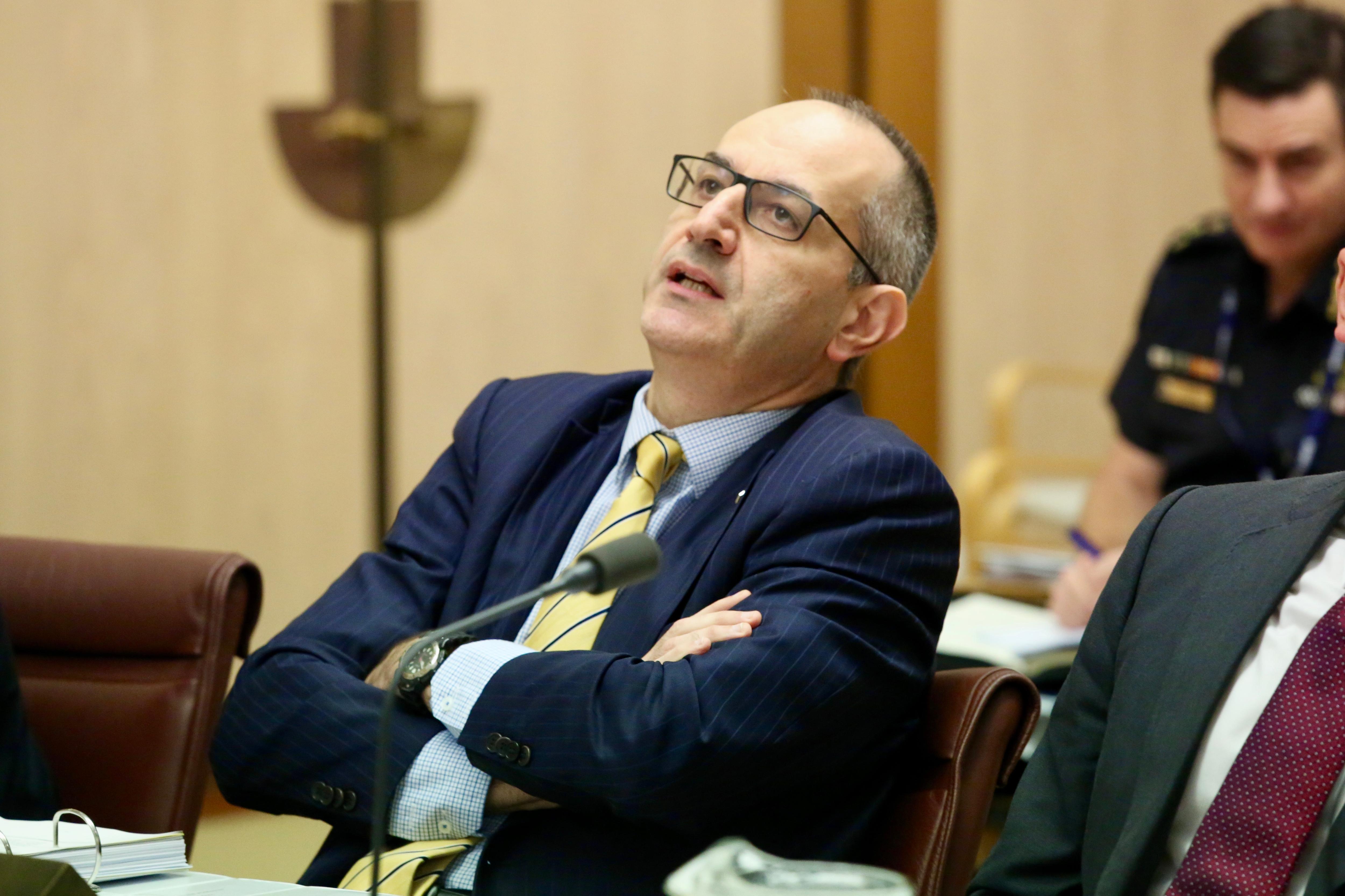Mike Pezzullo leans back with his arms crossed at a senate hearing