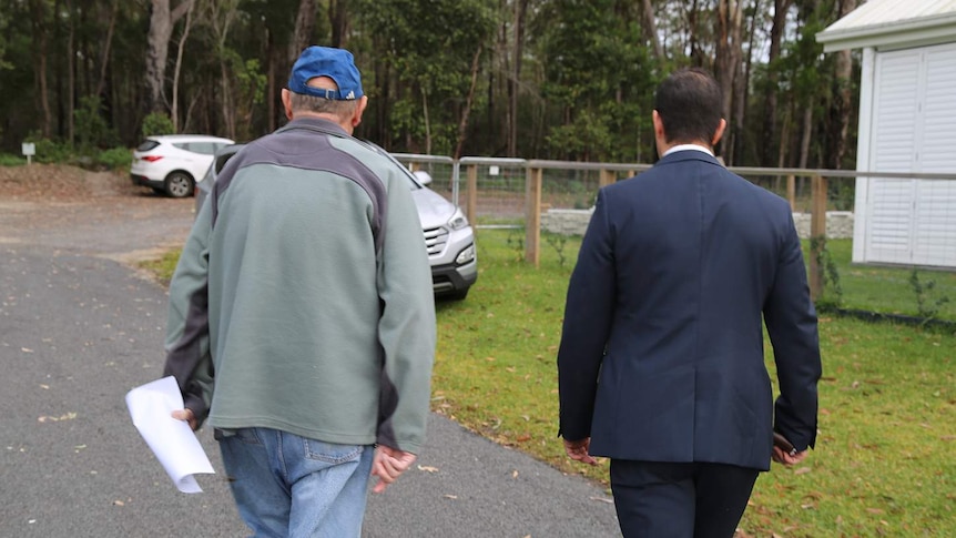 The back view of two men walking towards a car on a rural property