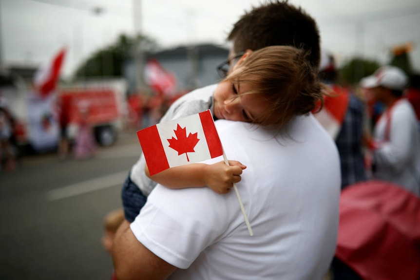 A child waves a Canadian flag while lying on a man's shoulder.