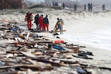 Debris covers sand on a beach as people can be seen gathered in the background. 