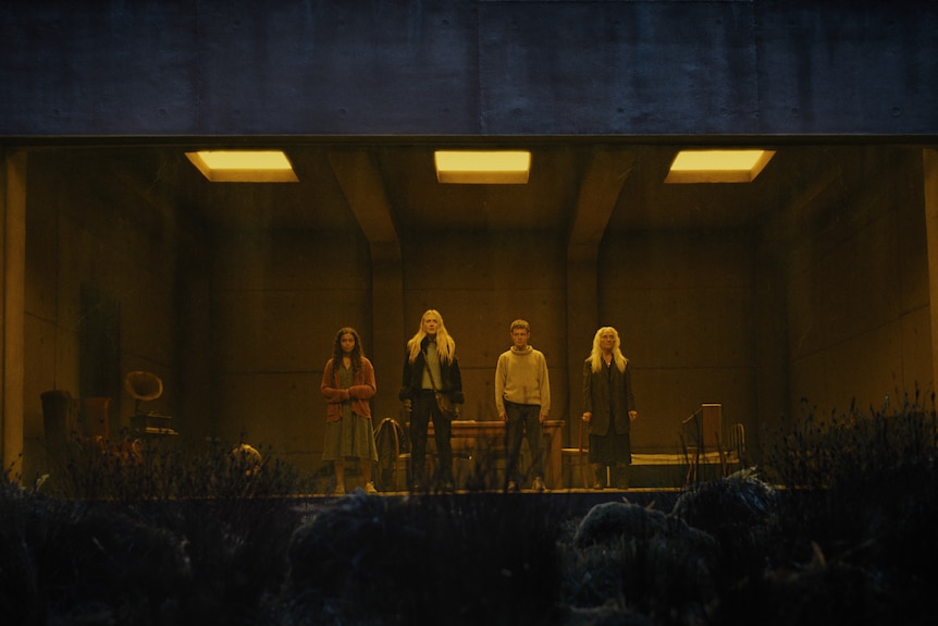 Four people stand inside a dimly lit concrete and glass room.