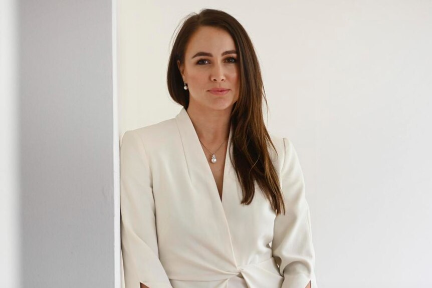 Woman in white suit leaning against wall with serious face