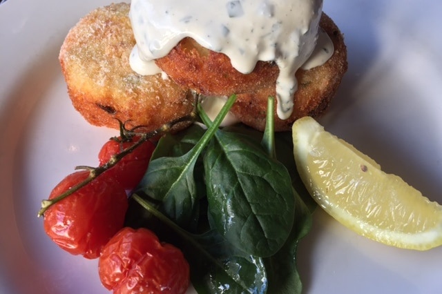 A plate of baby spinach, roasted baby tomatoes, potato hash cakes with a wedge of lemon.