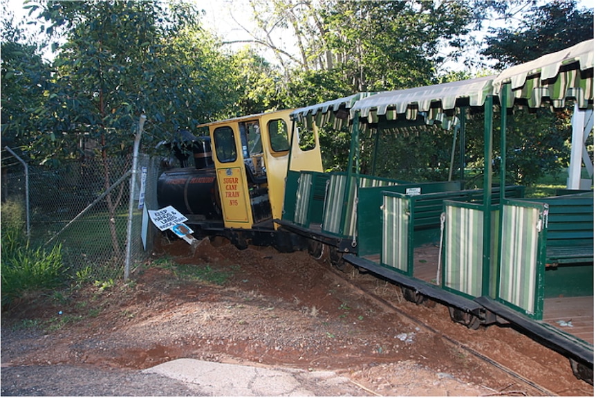 A derailed tourist train in a bushy area.