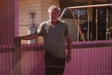 Man in tshirt stands in front of pink-stained corrugated iron fence 