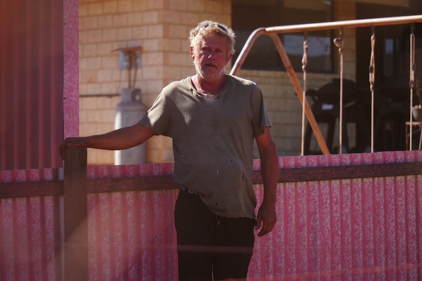 Man in tshirt stands in front of pink-stained corrugated iron fence 