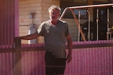 Man in tshirt stands in front of pink-stained corrugated iron fence 
