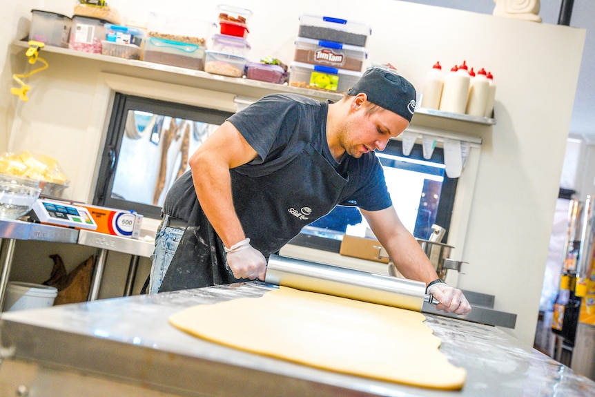 A man rolling out dough to make scrolls in a commerical kitchen