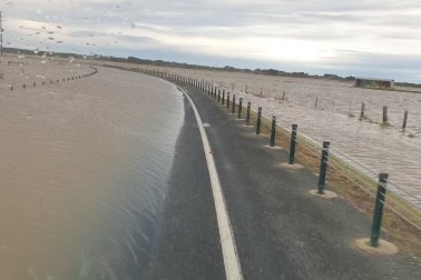 L'eau de crue couvre la majeure partie de la route, à l'exception de la ligne latérale droite et de la clôture, avec plus d'eau inondée de l'autre côté 