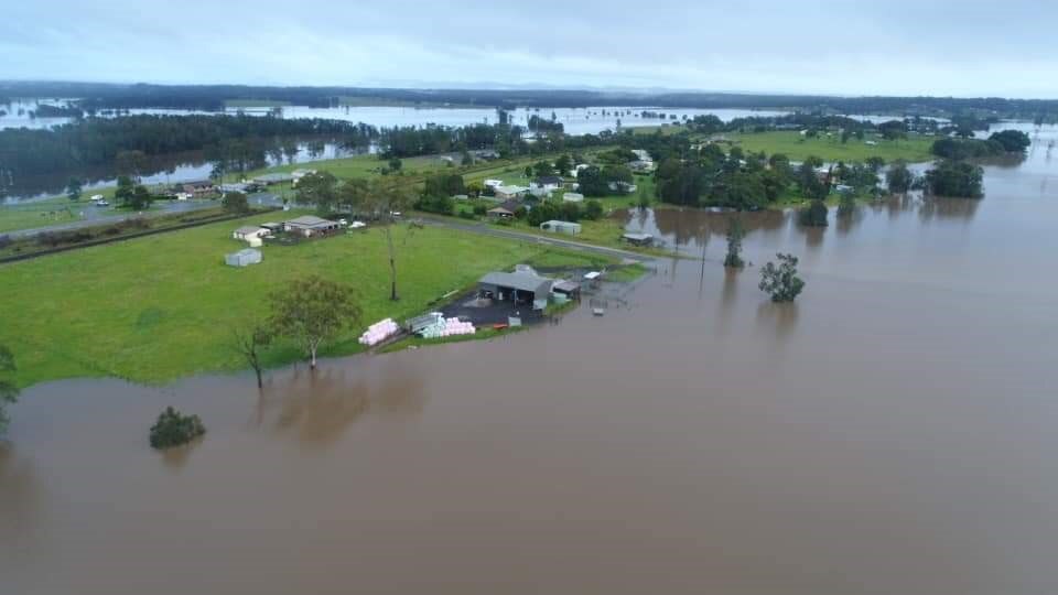 Drone shot of farm covered in brown floodwaters. The house is on a small island.