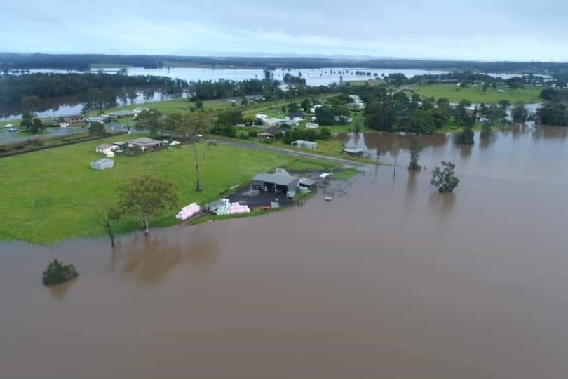 Drone shot of farm covered in brown floodwaters. The house is on a small island.